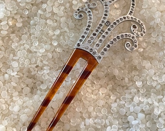 May include: A brown tortoiseshell hair comb with a silver and rhinestone decorative top. The comb has two prongs.