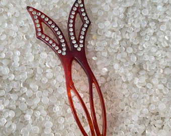 May include: A brown plastic hair comb with a decorative design featuring two wings with rhinestones. The comb is lying on a white background.