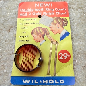 May include: Vintage hair accessory set on a yellow card. The set includes a double-tooth ring comb and two gold finish clips. The card features illustrations of women with hairstyles and text that reads "Double-tooth Ring Comb and 2 Gold Finish Clips!" and "WIL HOLD".