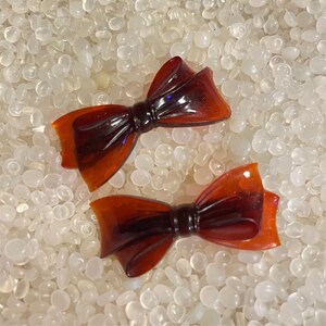 May include: Two brown plastic bow hair clips. The bows are translucent and have a dark brown centre.