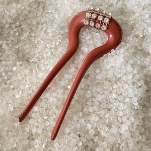 May include: A brown hair stick with a decorative rhinestone design. The stick is made of plastic and has a smooth, glossy finish.