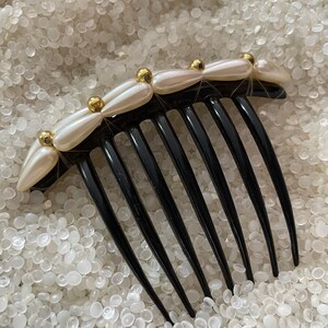May include: A black plastic hair comb with a decorative row of white pearlescent beads and gold accents.