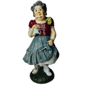 May include: A vintage figurine of an elderly woman in a red blouse and a blue-grey skirt, holding a handkerchief. The figurine has a detailed face, grey hair, and is standing on a green base. The woman is wearing white shoes.