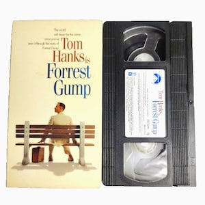 May include: A VHS tape and cover for the movie "Forrest Gump." The cover features the film's title and a man sitting on a bench. The VHS tape is black.
