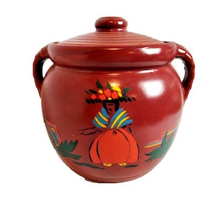 May include: A round, dark red ceramic jar with a matching lid and two side handles. The exterior features a hand-painted graphic of a figure wearing a blue and yellow shawl and a large orange skirt, accented by green leaves and small yellow flowers.