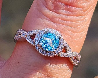 May include: A silver ring with a blue gemstone surrounded by smaller clear gemstones. The ring has a twisted band.