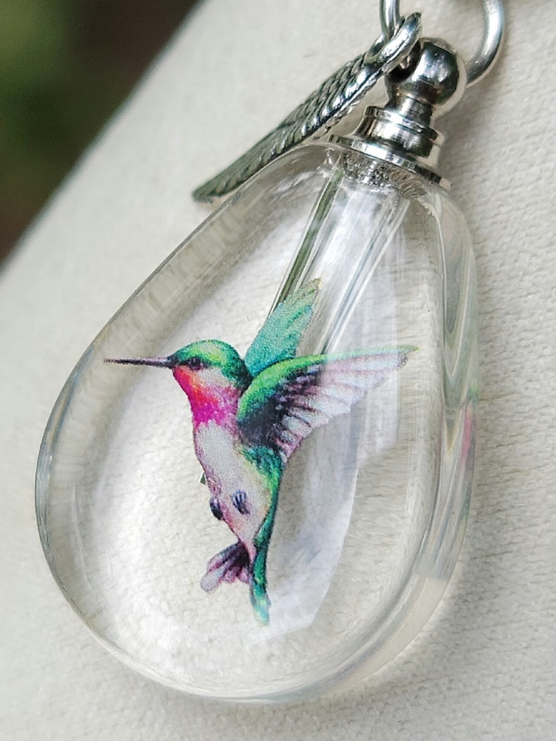 Puede incluir: Un colgante de cristal transparente en forma de l&aacute;grima con una cadena de plata y un dije de ala de plata. Dentro del colgante hay una imagen colorida de un colibr&iacute;.