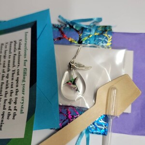 Puede incluir: Un dije de colibr&iacute; de vidrio transparente con alas plateadas, un peque&ntilde;o embudo de pl&aacute;stico, una cuchara de madera y un tubo de pl&aacute;stico transparente. Las instrucciones para llenar el dije est&aacute;n incluidas en una tarjeta azul.