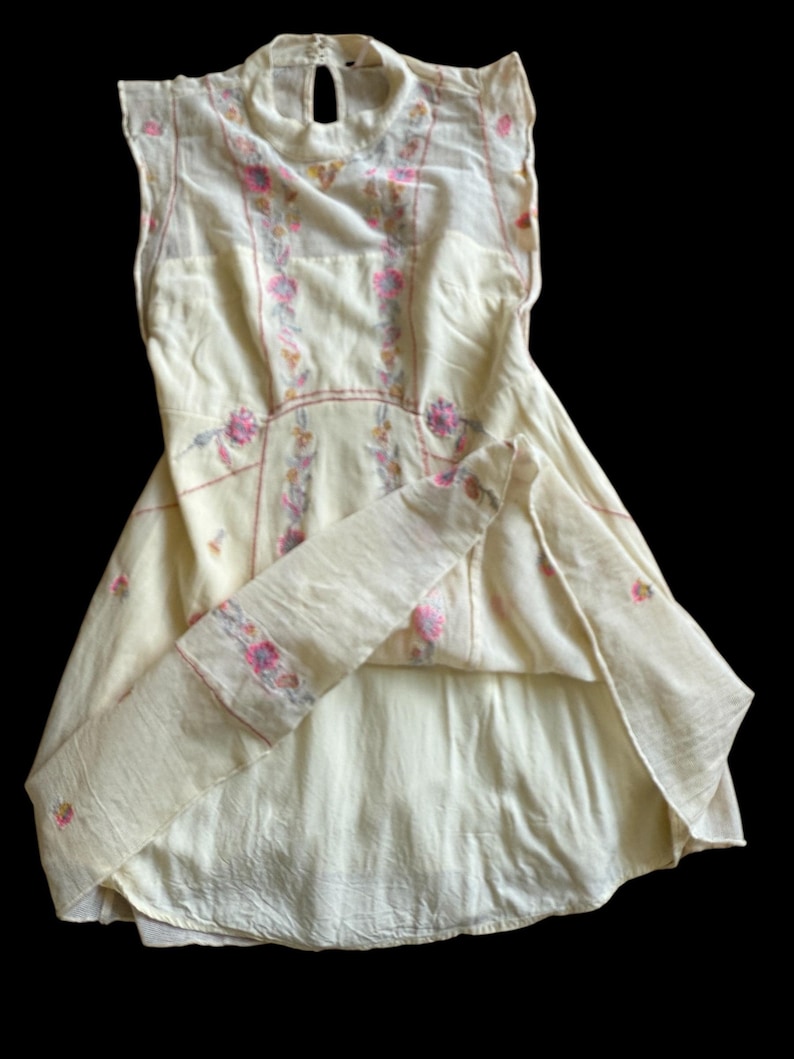 May include: A cream-colored vintage dress with floral embroidery in pink and yellow. The dress features a high neckline, keyhole back, and cap sleeves. The embroidery is concentrated on the bodice and along the seams, creating a delicate and feminine look.