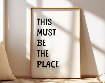 May include: A framed print with the text "THIS MUST BE THE PLACE" in black lettering on a white background.