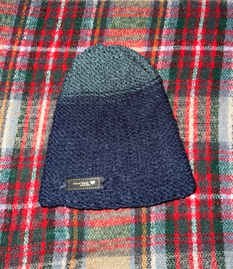 Peut inclure: Un bonnet en tricot bleu fonc&eacute; et turquoise avec une petite &eacute;tiquette brune qui dit "Hand Made with Love".