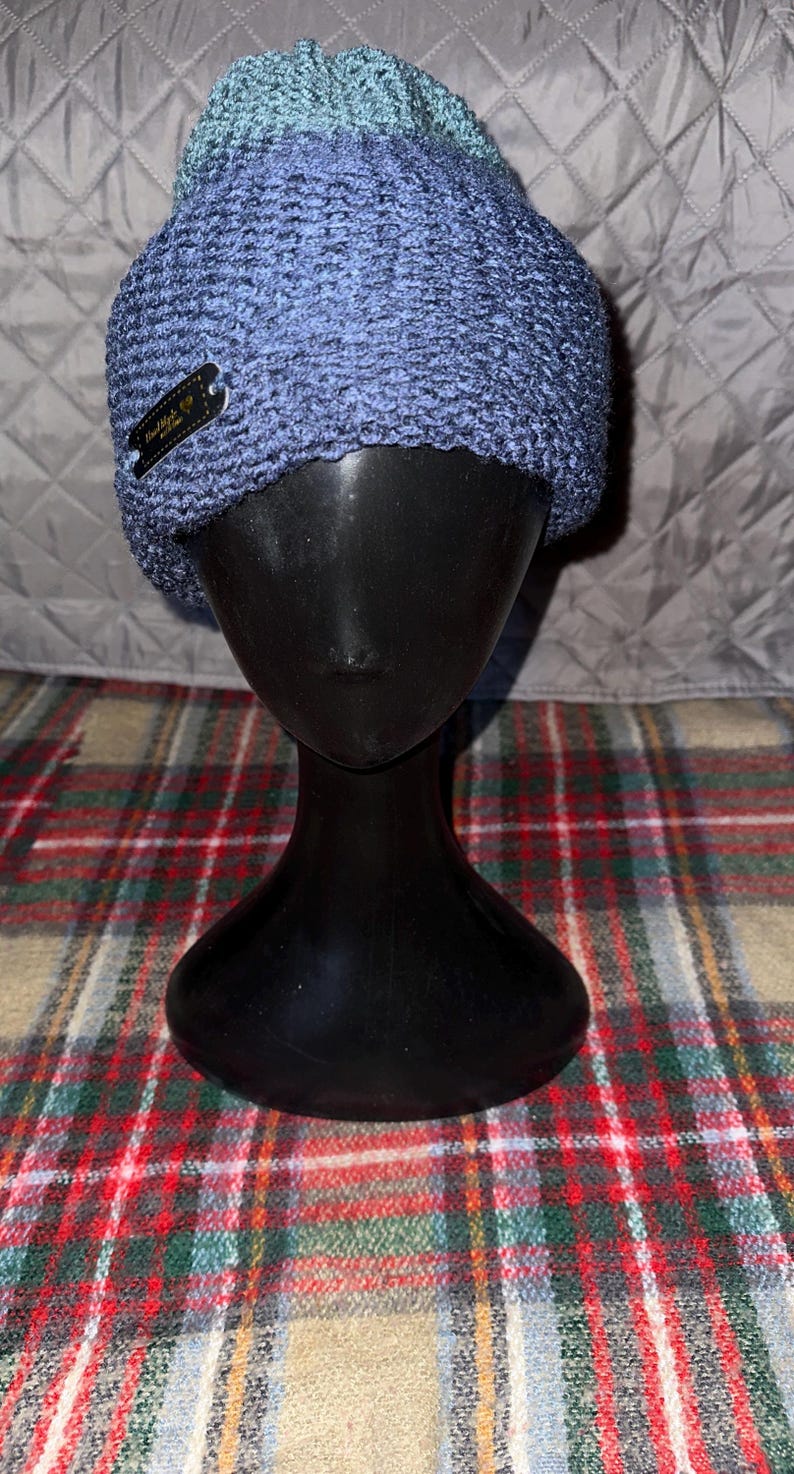 Peut inclure: Un bonnet en tricot bleu et vert avec une petite &eacute;tiquette noire indiquant "Oakland, CA".