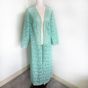 May include: A long, open-front robe in a delicate, floral lace pattern. The robe is a soft, mint green color with a scalloped edge trim. The robe is displayed on a mannequin.