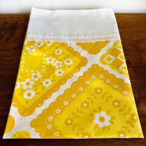 May include: A vintage pillowcase with a bright yellow floral pattern. The pillowcase features a white top with a delicate lace trim. The yellow portion has a repeating pattern of white flowers and geometric shapes, creating a cheerful, retro aesthetic.