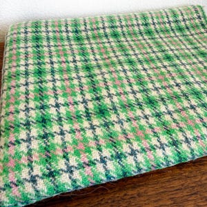May include: A folded fabric with a green, pink, and navy blue plaid pattern. The fabric has a textured appearance and is likely wool or a similar material. The plaid design is a classic pattern, suitable for various sewing projects.