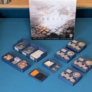 May include: The board game "Brass: Birmingham" is displayed with blue plastic organizers for game components. These organizers contain cards, wooden tokens, and metal coins. The game is set on a blue surface.