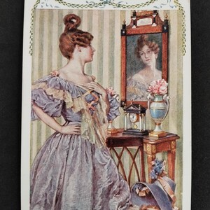 Puede incluir: Una mujer con un vestido lavanda se encuentra de pie frente a un espejo, mirando su reflejo. El espejo tiene un marco adornado y hay un reloj en la mesa debajo. Hay un sombrero en el suelo junto a la mesa.