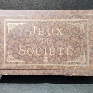 Puede incluir: Una caja de madera marrón con una inscripción dorada que dice "Jeux de Société".