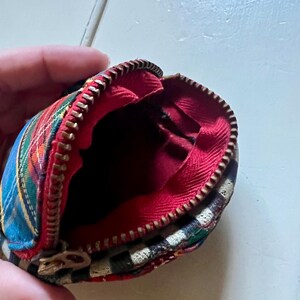 May include: Small, open coin purse with a tartan pattern in red, blue, green, and yellow. The interior is red, and the zipper is gold-coloured. The purse is round, with a vintage aesthetic.