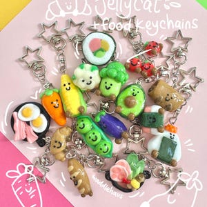 Puede incluir: Una colección de llaveros caprichosos con temática de comida, que incluyen sushi, aguacate, maíz y guisantes. Cada llavero es de colores brillantes y presenta una cara sonriente. Los llaveros están sujetos a cierres plateados en forma de estrella.