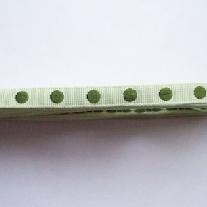 May include: A close-up of a white ribbon with green polka dots. The ribbon is folded and appears to be made of a woven fabric.