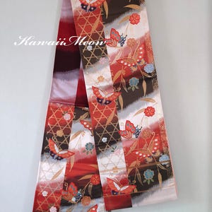 May include: A decorative textile with a repeating butterfly and floral pattern in red, brown, and white. The textile features a mix of geometric and organic designs, with the text "Kawaii Meow" in the upper left corner.