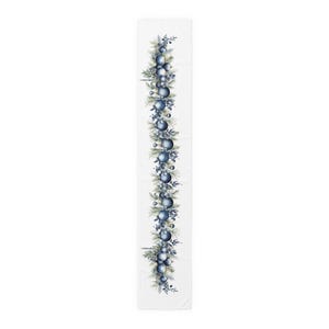 May include: A white table runner featuring a vertical design of blue ornaments, berries, and evergreen sprigs. The festive pattern is arranged in a linear fashion, creating a decorative accent for holiday tables. The runner is approximately 72 inches long.