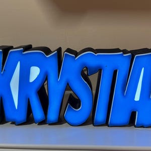 May include: A blue light-up sign with the name "Krystan" in a bold, graffiti-style font.