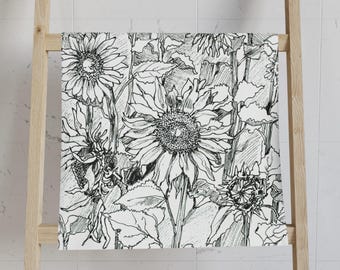 May include: A white and black hand-drawn sunflower design on a towel. The towel is draped over a wooden ladder. The sunflowers are in various stages of bloom, with detailed leaves and stems.