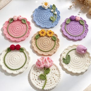 May include: Seven circular crochet coasters featuring floral designs. Each coaster has a scalloped edge and is decorated with various crocheted flowers and green leaves, including roses, daisies, sunflowers, and tulips in pink, blue, purple, and white.