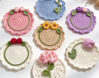 May include: Seven circular crochet coasters featuring floral designs. Each coaster has a scalloped edge and is decorated with various crocheted flowers and green leaves, including roses, daisies, sunflowers, and tulips in pink, blue, purple, and white.