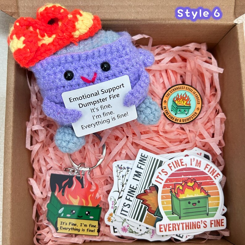 Peut inclure: Un kit de crochet sur le th&egrave;me du "dumpster fire" de soutien &eacute;motionnel. Le kit comprend une peluche de feu de poubelle au crochet violet, des autocollants et un porte-cl&eacute;s. La peluche a une fleur rouge et jaune sur le dessus et une pancarte avec le texte "It's fine, I'm fine. Everything is fine!"