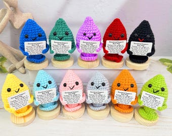 May include: A collection of colorful, handmade crochet butt plugs, each with a smiling face and a small sign that reads "Emotional Support Butt Plug." The plugs are in various colors, including blue, green, purple, red, and black.
