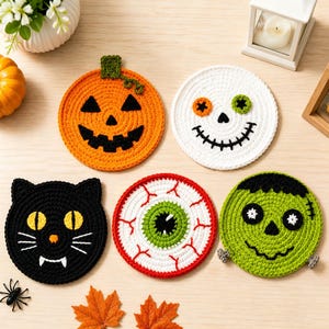 Puede incluir: Cinco posavasos redondos de ganchillo con diseños de Halloween: una calabaza naranja, una calavera blanca con ojos desiguales, una cara de gato negro, un globo ocular blanco con venas rojas e iris verde, y una cara de monstruo verde.