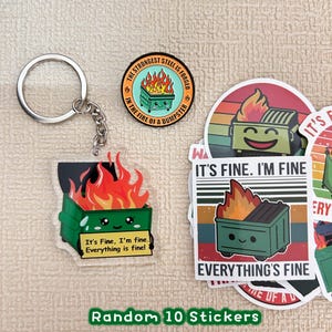 Peut inclure: Un ensemble d'autocollants, un porte-cl&eacute;s et un badge repr&eacute;sentant une poubelle verte en feu avec un visage souriant. Le texte sur les articles se lit "It's Fine, I'm fine. Everything is fine !" et "The strongest steel is forged in the fire of a dumpster."