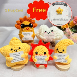 May include: Five crocheted plush toys, each with a different design and a message. The toys are a sun, a cloud, a star, a sun, and a moon. Each toy is holding a small card with a positive message. The messages are: "Positive Sunshine I may be a ray of sunshine, but I believe in you. Rise & Shine Smile & Be Awesome!"  "Emotional Support Cloud You're cirrus-ly awesome I cirrus-ly love you!"  "Positive Star I may be a tiny star, but I believe in you. Go do your thing!"  "Positive Sunshine I may be a ray of sunshine, but I believe in you. Rise & Shine Smile & Be Awesome!"  "Positive Moon I may be a tiny moon, but I believe in you. Go do your thing!"
