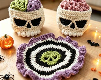 May include: Two cream-colored crocheted skull baskets with textured brain-like tops in green, purple, and pink, accompanied by a round, ruffled crocheted doily featuring a central green skull motif surrounded by concentric black, white, and purple rings.