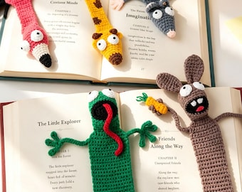 May include: Five crocheted animal bookmarks shaped like a pink flamingo, a yellow giraffe, a gray mouse, a green frog with a long red tongue, and a brown rabbit holding a small orange carrot, all resting on open book pages with visible text.