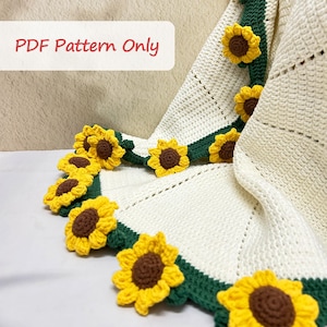 K&ouml;nnte beinhalten: Eine wei&szlig;e H&auml;keldecke mit gr&uuml;nem Rand und geh&auml;kelten Sonnenblumen-Applikationen. Die Decke ist in der H&auml;lfte gefaltet und die Sonnenblumen sind am Rand der Decke sichtbar. Der Text "PDF Pattern Only" ist in der oberen linken Ecke des Bildes sichtbar.