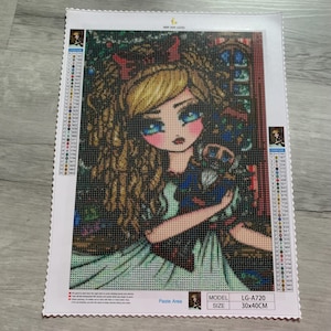 Puede incluir: Kit de pintura de diamantes con una niña de dibujos animados con cabello rubio, ojos azules y un lazo rojo. La obra de arte está ambientada en un fondo de vidrieras. El tamaño del kit es de 30x40cm.