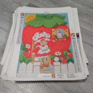 Puede incluir: Un montón de kits de pintura de diamantes con una imagen de dibujos animados de una niña en una casa de fresas. La obra de arte incluye una fresa roja, hojas verdes y una valla blanca. El tamaño es de 30x40cm.