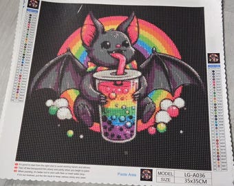 Puede incluir: Kit de pintura de diamantes con un murciélago de dibujos animados con un arcoíris y una bebida colorida. El murciélago tiene alas negras y una lengua rosa. El kit mide 35x35cm.