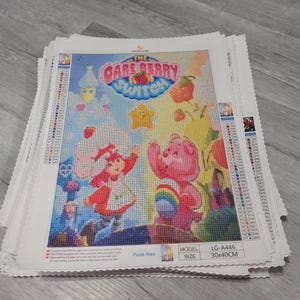 May include: A stack of diamond painting kits featuring Care Bears characters. The kits are white with a colorful image of the Care Bears characters, including Care-a-lot Bear and Cheer Bear. The image is surrounded by a pink, blue, and yellow border. The text "The Care Berry Switch" is printed in the center of the image. The kits are labeled with the model number "LG-A446" and the size "30x40CM".