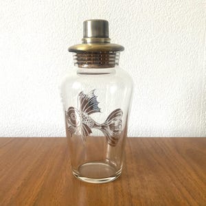 Vintage glass decanter, decorated with a fish, has a silver plated lid