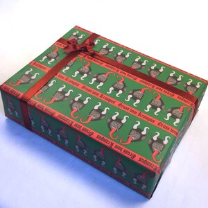 May include: Green gift wrap with a repeating pattern of red-tongued, horned creatures with the text "Gruss vom Krampus" in red gothic lettering. The gift is tied with a red ribbon.