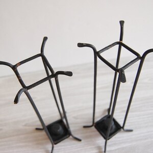 Puede incluir: Dos candelabros de metal negro con base cuadrada y parte superior cuadrada. Los candelabros est&aacute;n hechos de metal delgado y tienen un aspecto r&uacute;stico.