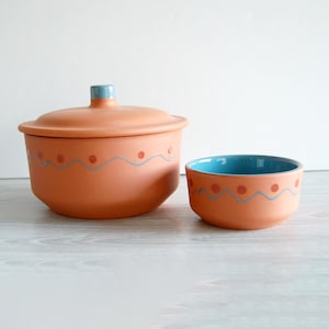 May include: A terracotta serving bowl with a lid and a smaller terracotta bowl. Both bowls have a blue and red wavy design with red dots.