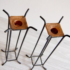 Puede incluir: Un juego de dos candelabros de metal negro con portavelas de cobre. Los candelabros tienen una base cuadrada y cuatro patas.