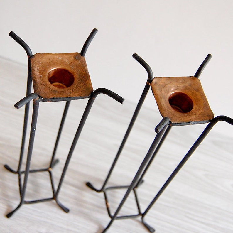 Puede incluir: Un juego de dos candelabros de metal negro con portavelas de cobre. Los candelabros tienen una base cuadrada y cuatro patas.