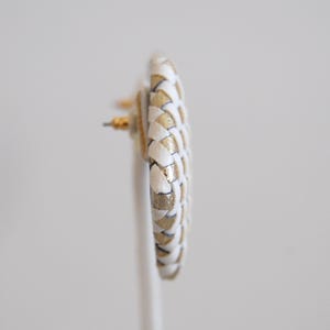 Op de afbeelding: Een paar witte en gouden geweven creolen. De oorbellen zijn gemaakt van een gevlochten materiaal met een gouden accent.
